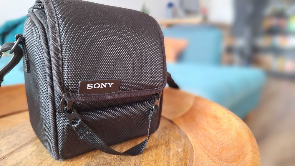 Eine Objektivtasche im Test in Nahaufnahme steht auf einem Holztisch im Hintergrund ein Wohnzimmer.