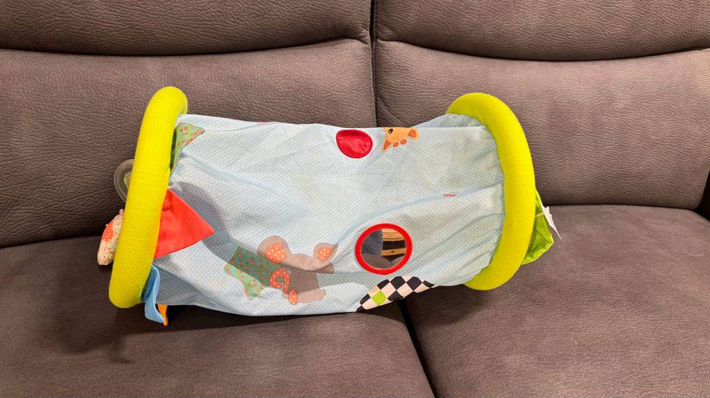 Eine bunte, getestete Krabbelrolle liegt auf einem braunen Sofa.