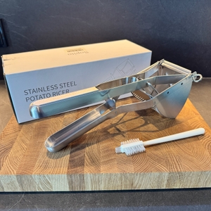 Sopito-Kartoffelpresse, Reinigungsbürste und Karton auf einem Holzbrett.