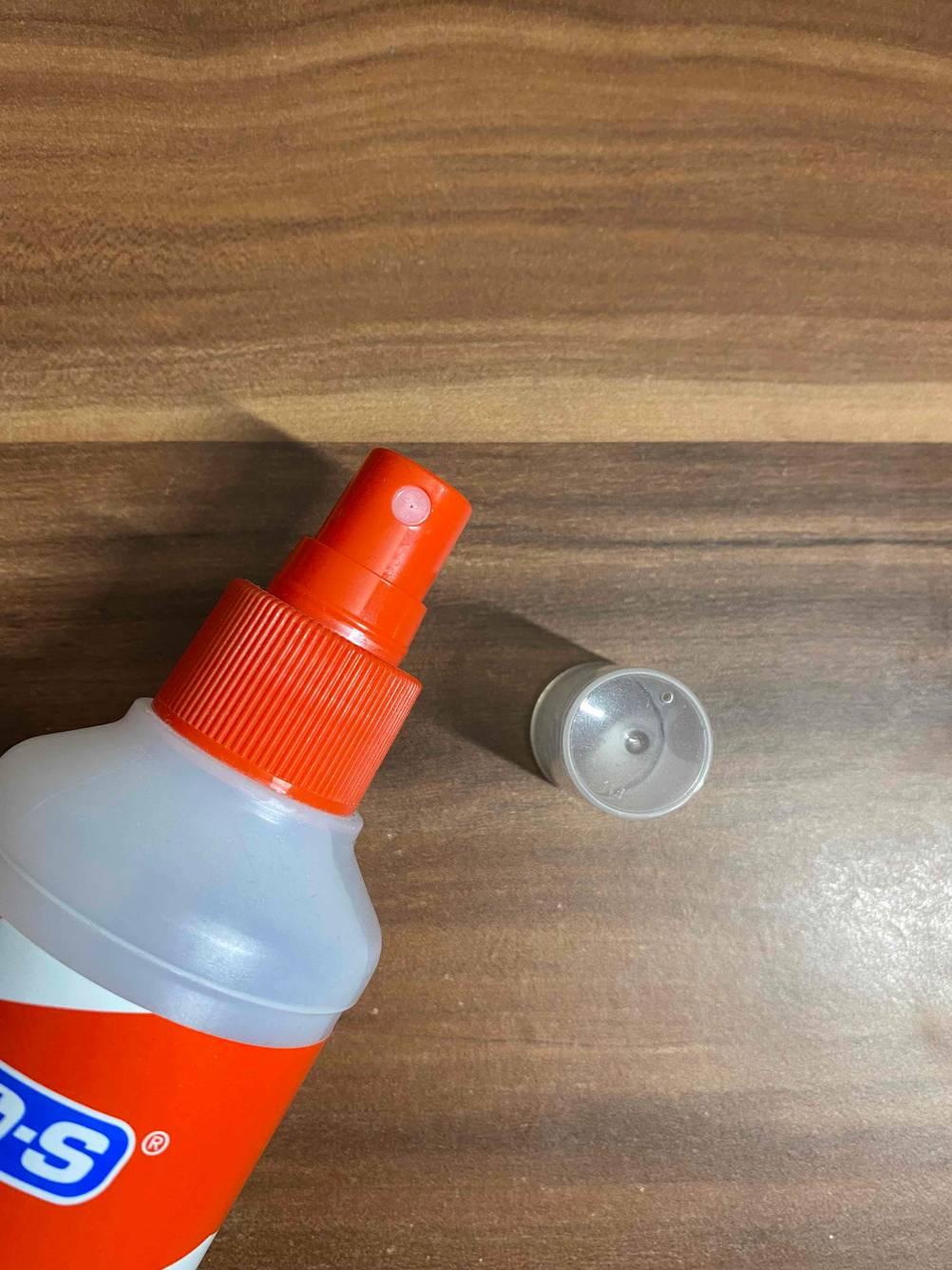 Detailansicht der Sprühdüse einer geöffneten Flasche Fußpilz-Spray, der Deckel liegt im Hintergrund auf einer Holzfläche.