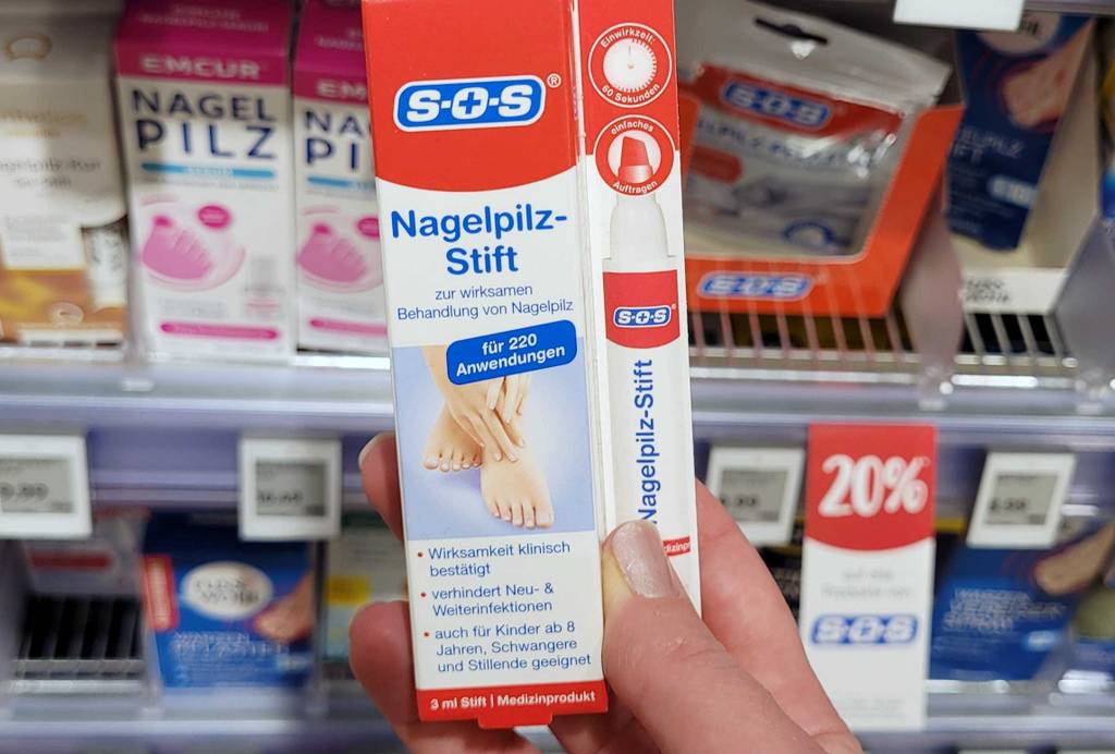 Eine Hand hält eine Packung Nagelpilzlack als Stift zum Testen.