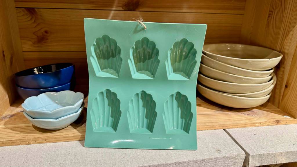 Eine getestete Madeleine-Backform steht zwischen Porzellanschalen in einem Regal.
