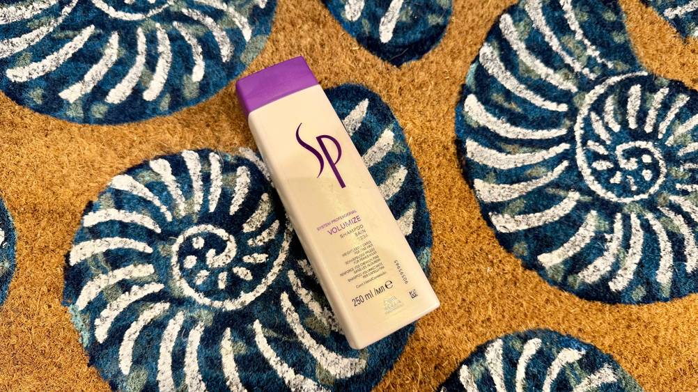 Auf einem Teppich mit Schneckenhäusern liegt eine Flasche des getesteten SP-Shampoos.