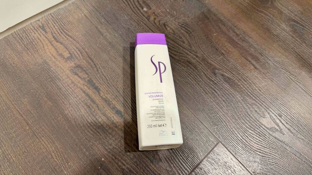 Eine Flasche des getesteten SP-Shampoos liegt auf einem Holzboden.
