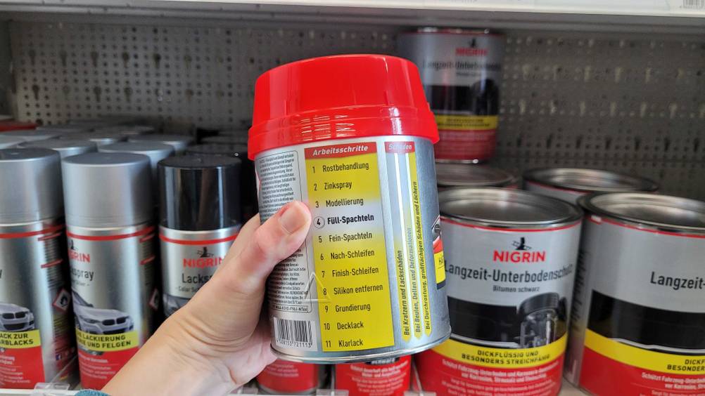 Eine Dose mit Arbeitsschritten zu einer getesteten Spachtelmasse für das Auto befindet sich in einer Hand.