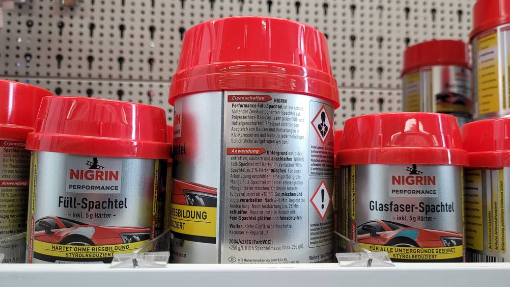 Rückseite von einer Dose mit getesteter Spachtelmasse für das Auto steht auf einem Regal. 