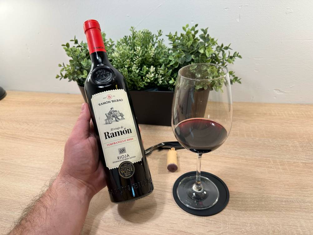 Eine Hand hält eine Flachen des spanischen Rotweins neben ein Glas mit Wein, im Hintergrund ein Topf mit Pflanzen.