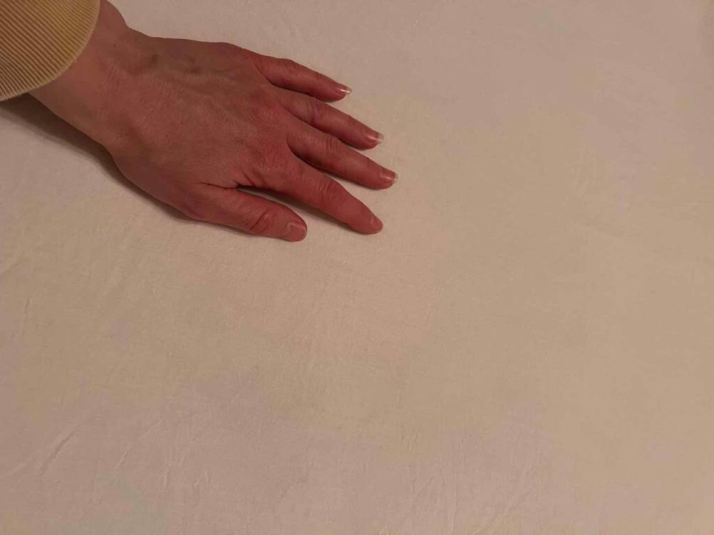 Eine Hand streicht über ein getestetes weißes Spannbettlaken in 180 x 200 cm.