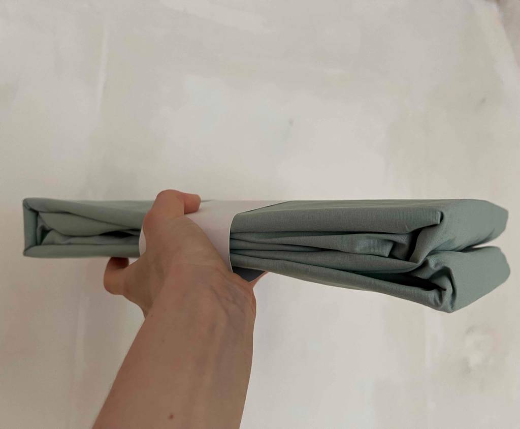 Spannbettlakens 180 x 200 cm im Test: Hand hält ein verpacktes Spannbetttuch vor weißer Wand.