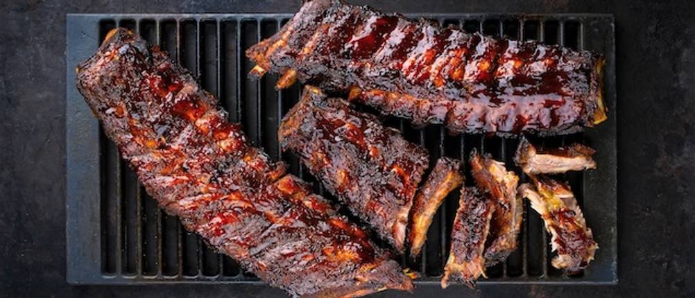 Spareribs-Halter getestet: Mehrere Spareribs liegen auf einem Grillrost und ragen darüber hinaus.