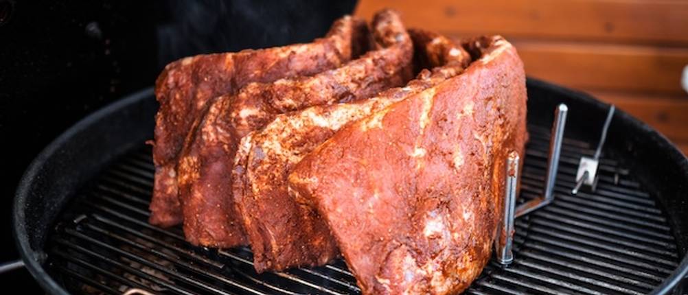 Spareribs-Halter-Test: Mehrere Fleischstücke stehen in einem Ständer auf einem Grill.