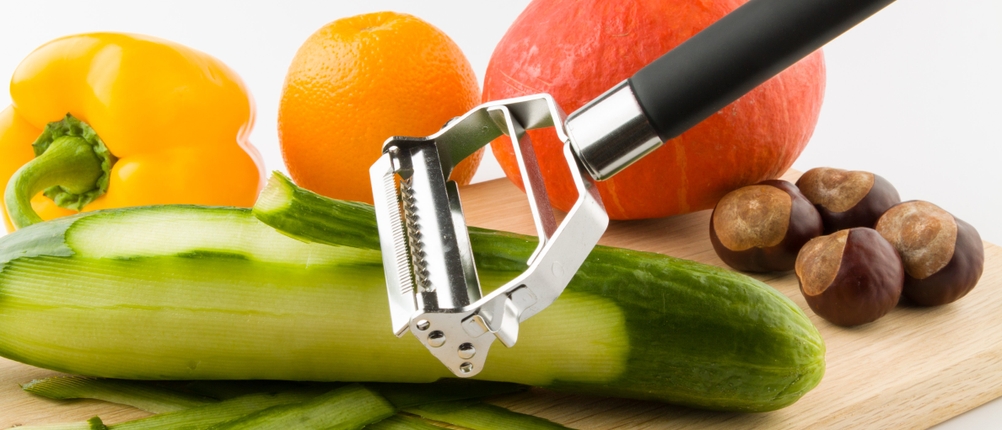 Eine Gurke wird auf einem Brett geschält, dahinter liegen andere Lebensmittel.