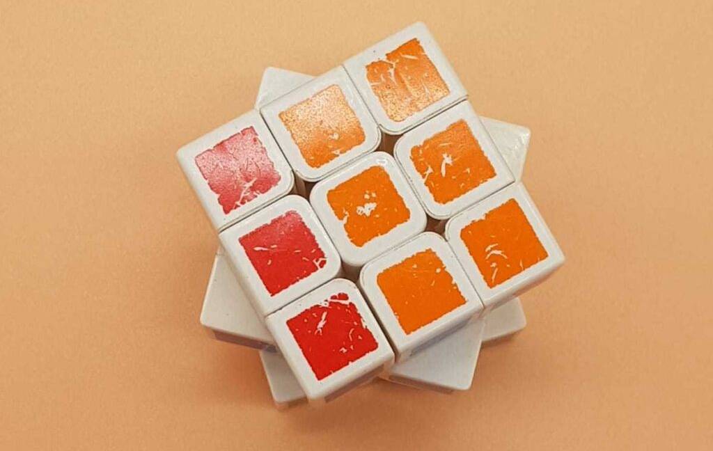 Im Test: ein Speedcube, gedreht, mit roter und orangefarbenen Feldern in einer Reihe vor einem pfirsichfarbenen Hintergrund.
