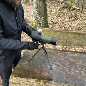 Ein Nutzer in schwarzer Outdoor-Kleidung stellt das Gosky 20-60x60 Spektiv auf einem Stativ ein. Das Gerät steht stabil auf einer Holzbank.