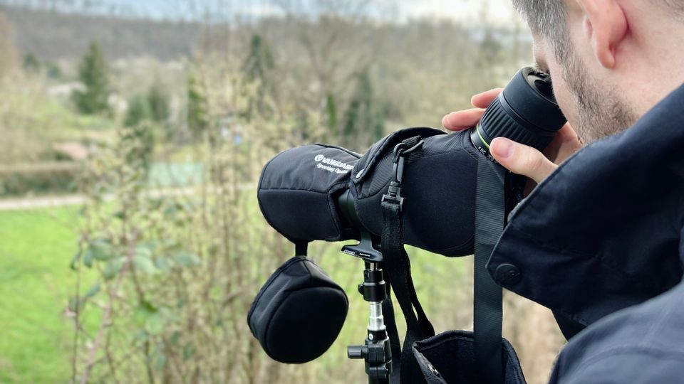 Ein Mann blickt durch das Vanguard Endeavor HD 82A Spektiv in einer Waldlandschaft. Das Spektiv steht auf einem Stativ mit montierter Schutzhülle.