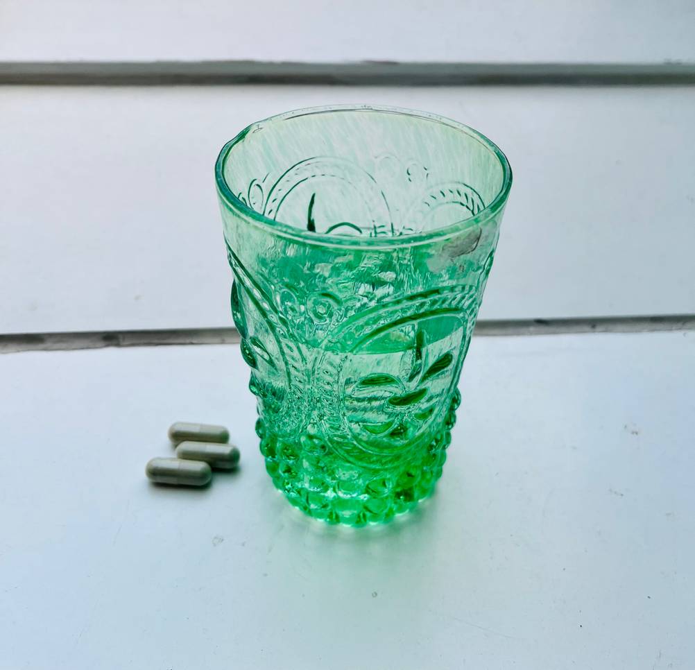 Spermidin-Kapseln getestet: Neben einem grünen Wasserglas liegen drei Kapseln auf einer hellen Fläche.