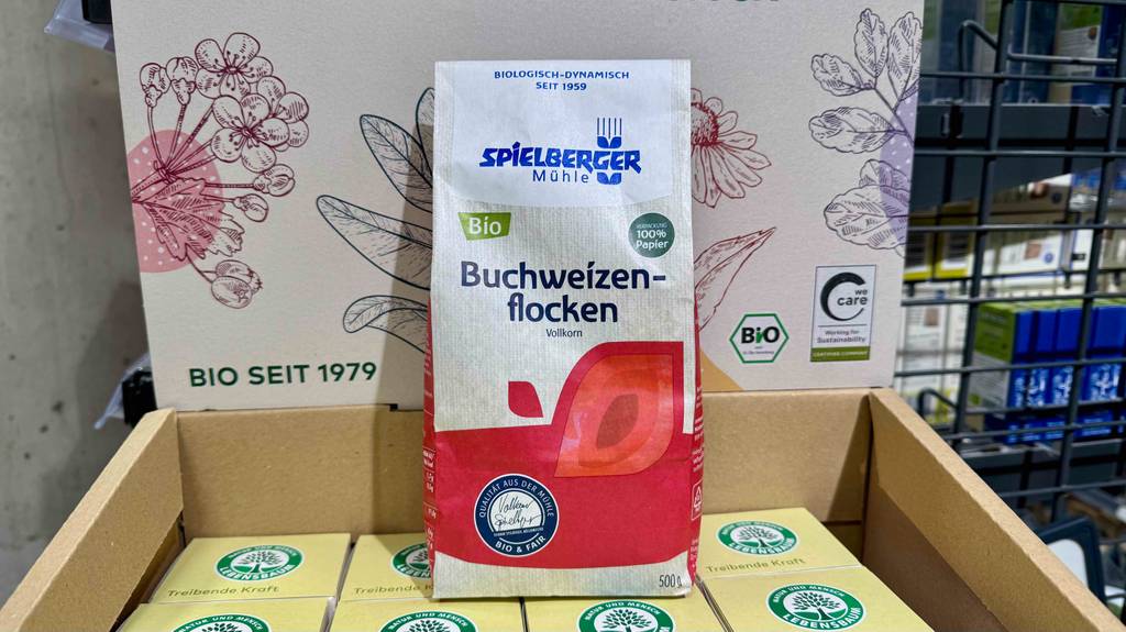 Die getesteten Buchweizenflocken in einer 500-g-Packung stehen auf einem Karton mit Lebensmitteln.