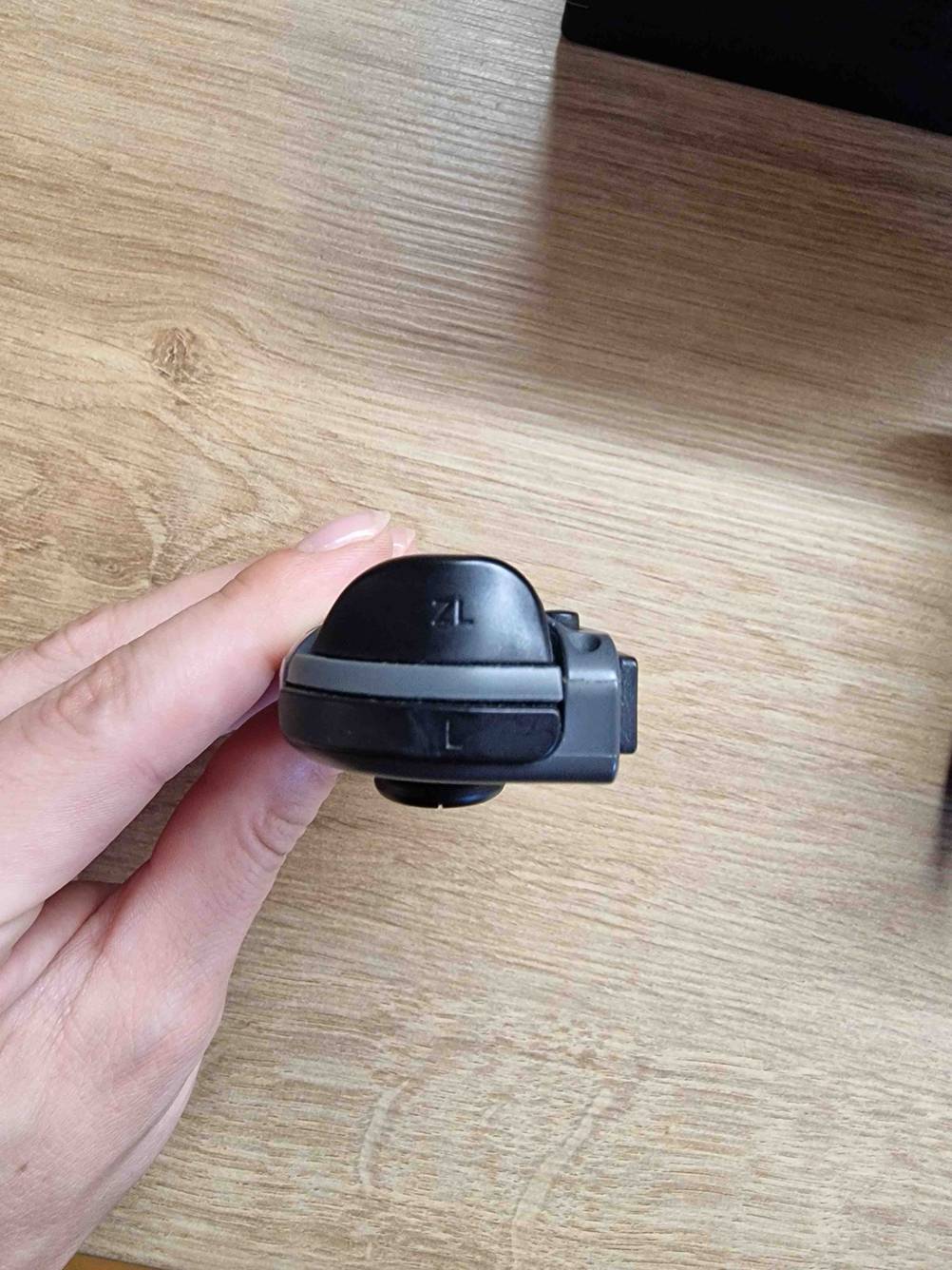 Nahaufnahme der Bedienknöpfe an einer Spielekonsole die eine Hand vor einen Holztisch hält.