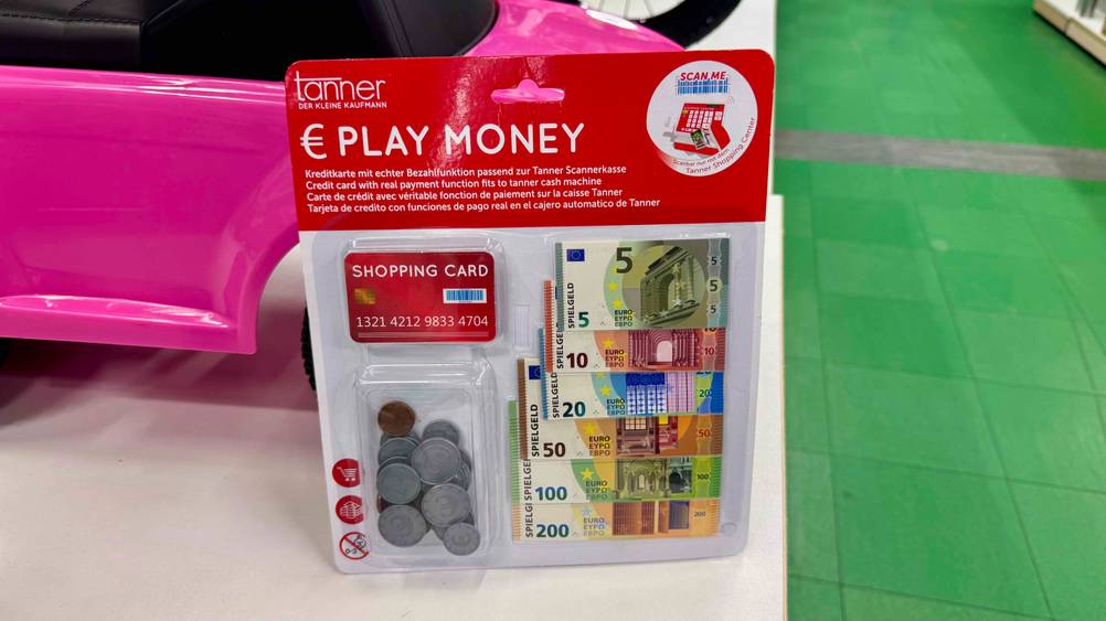 Eine Packung des Spielgeldes im Test lehnt an einem Spielzeugauto.