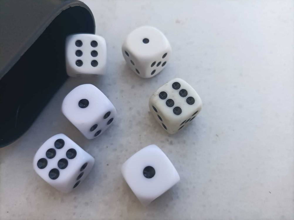 Mehrere unterschiedliche Spielwürfel im Test vor einem Becher.