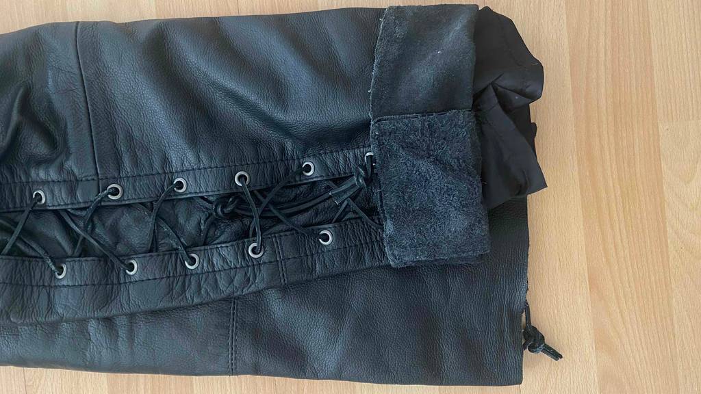Lederhosen-Test: Detailansicht der unteren Bein-Schnürung einer schwarzen Lederhose auf einem Parkettboden.