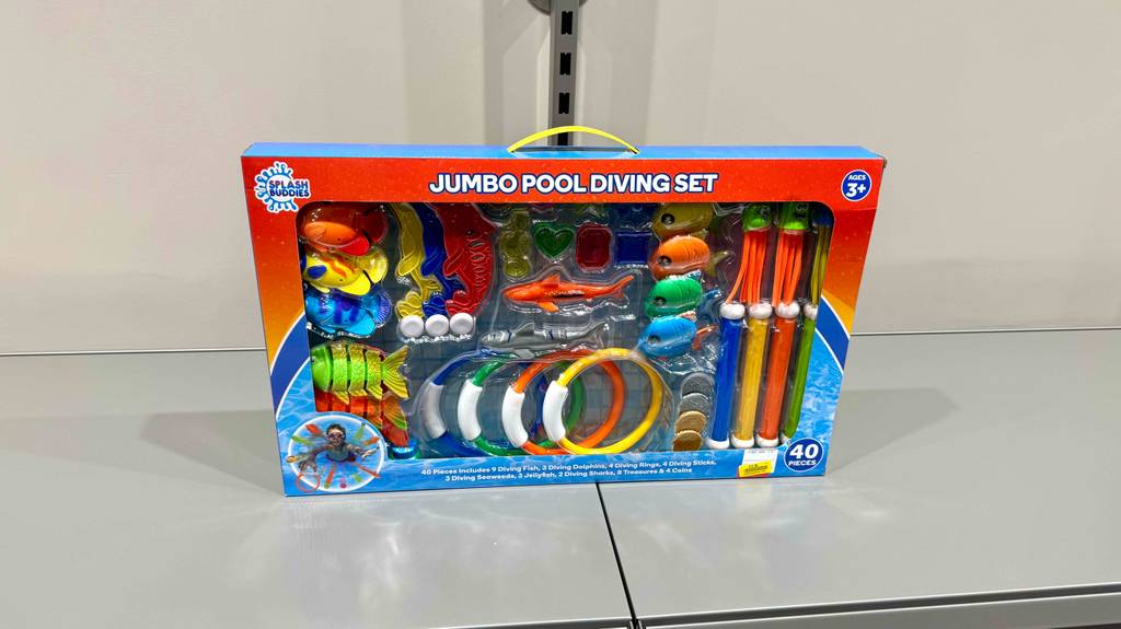 Das getestete Tauchspielzeug bestehend aus 40 bunten Einzelteilen steht innerhalb seiner Verpackung auf einem weißen Regal.