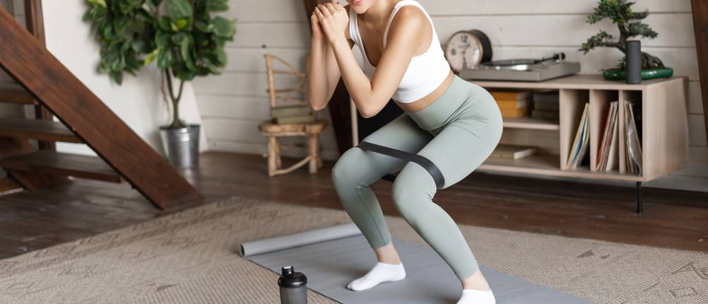 Sportleggings im Test: Frau mit grüner Leggings macht zuhause ein Workout.