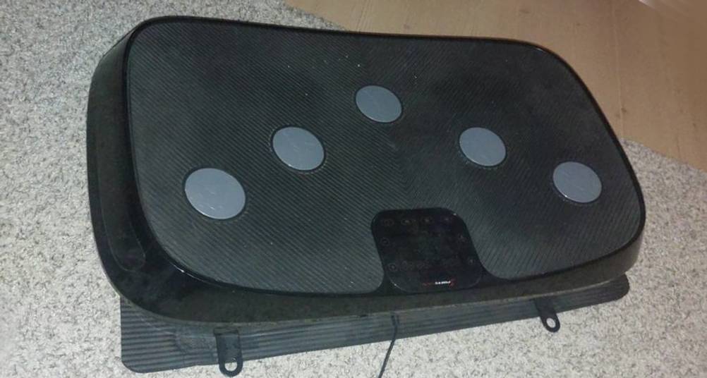 Vibrationsplatten-Test: eine schwarz-graue Vibrationsplatte inklusive 3D-Vibration und LCD-Anzeige befindet sich ausgeschaltet auf einem hellgrauen Teppichboden.