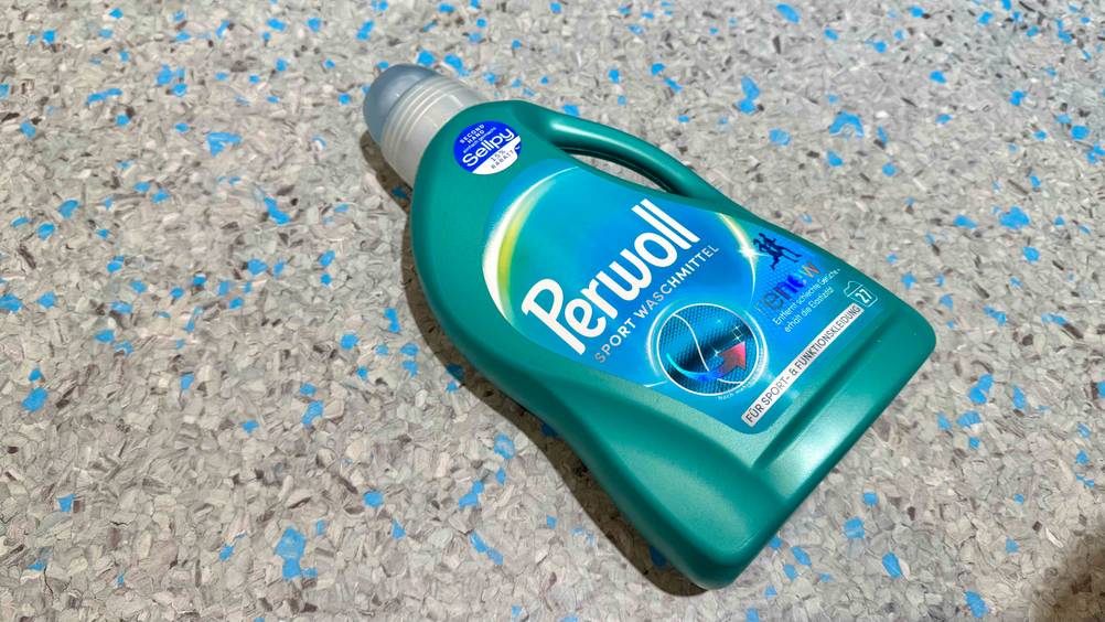 Sportwaschmittel getestet: Eine Flasche liegt leicht horizontal auf einem grau-blauen Boden.
