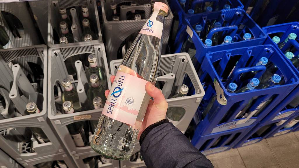 Im Test: Eine Hand hält Mineralwasser in der Glasflasche über Getränkekisten.