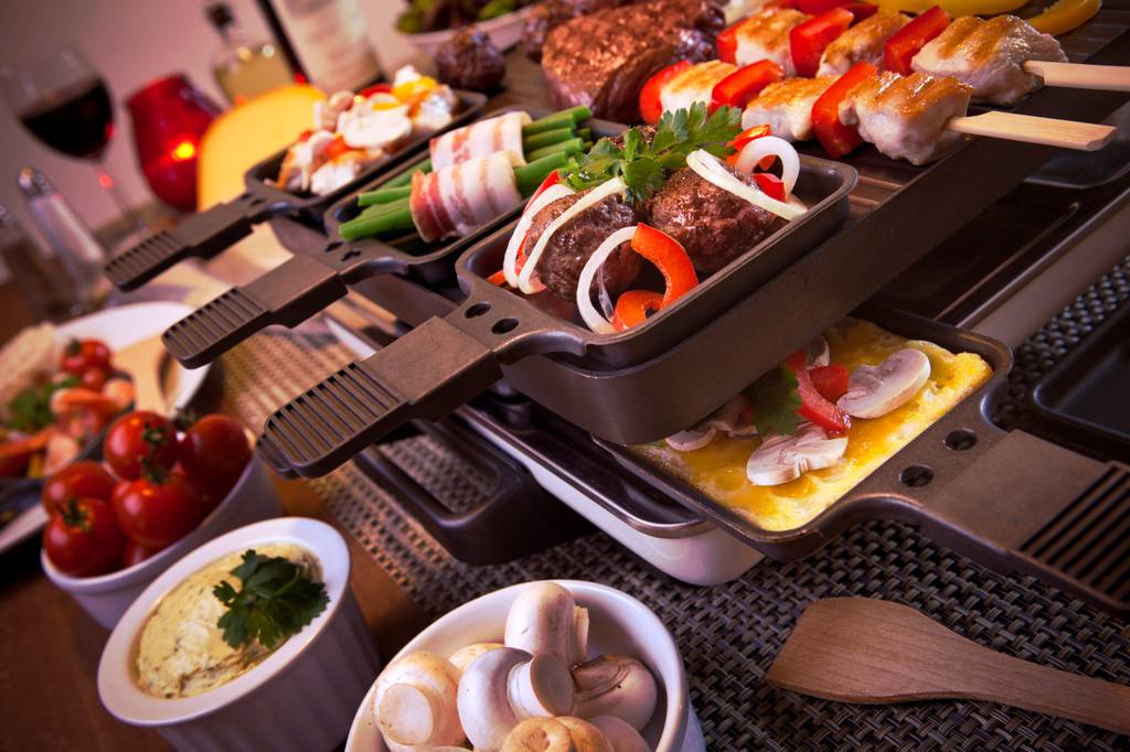 Spring-Raclette-Test: Mehrere Raclette-Pfännchen sind mit verschiedenen Zutaten gefüllt und stehen auf einem Raclette. 