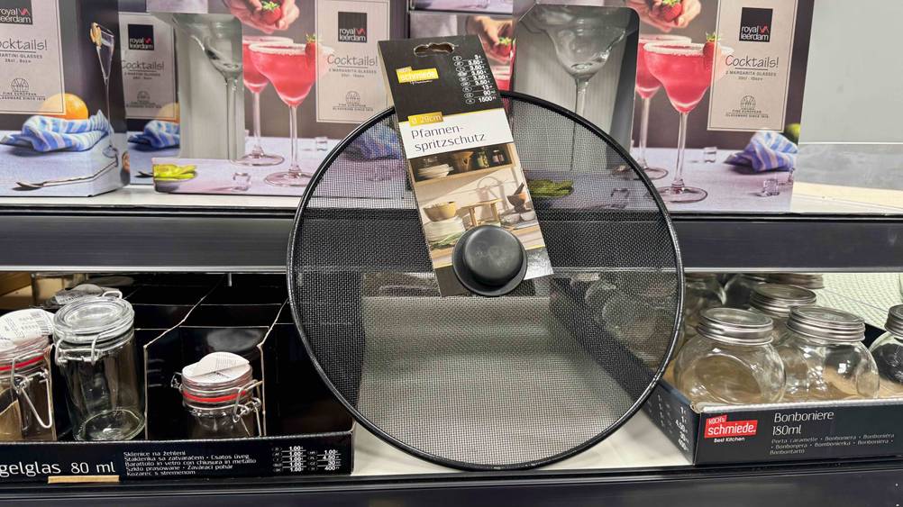 Ein getesteter Spritzschutz für Pfannen steht vor einem Regal.