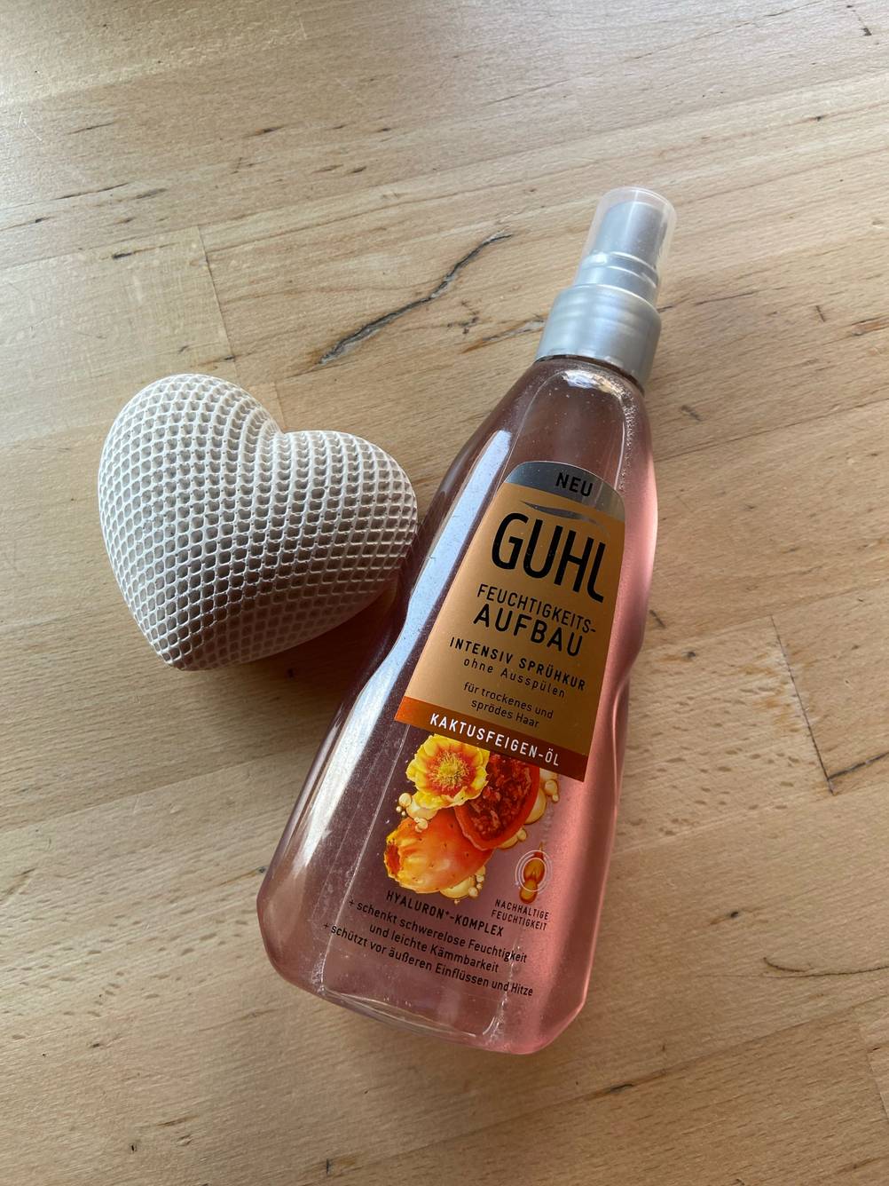 Auf einer Holzfläche neben einem Herz liegt eine Flasche der getesteten Sprühkur.