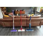 Drei Sprühwischer stehen nebeneinander vor einem Sofa.