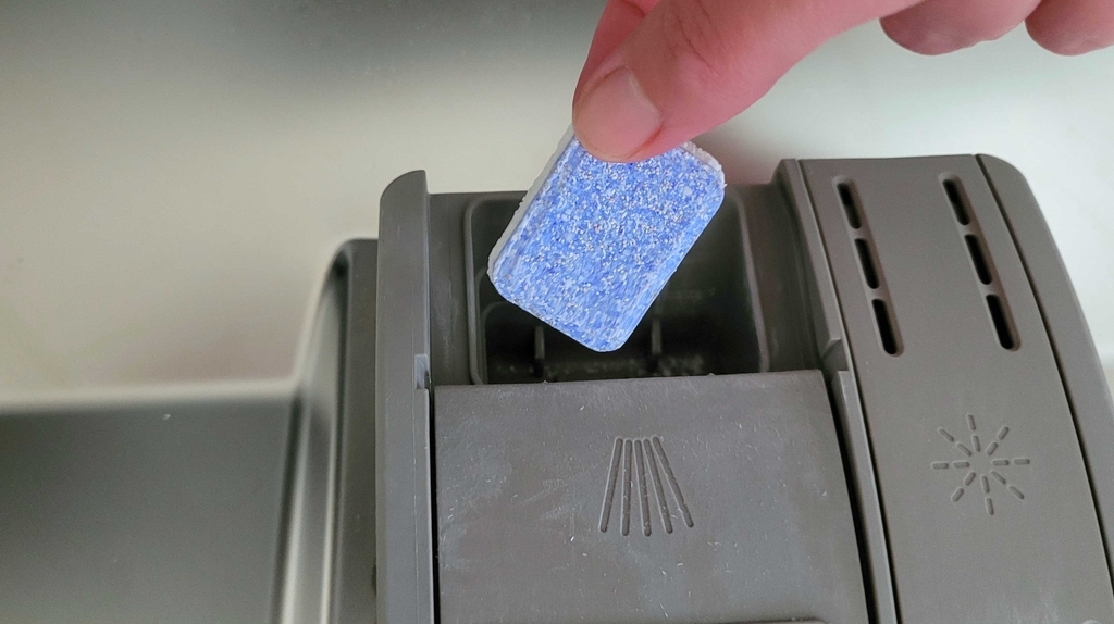 Eine Hand legt ein ausgepacktes Tab in das Fach der Geschirrspülmaschine.