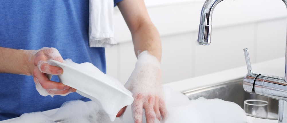 Spülmittel-Test: Ein Mann spült mit viel Schaum Geschirr.