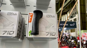An einem Verkaufsregal im Sportartikel-Verkaufsbereich ist vor mehreren in weißen Verpackungen mit SQ-lab MTB-Griffen ein schwarzer getesteter MTB-Griff ausgestellt.