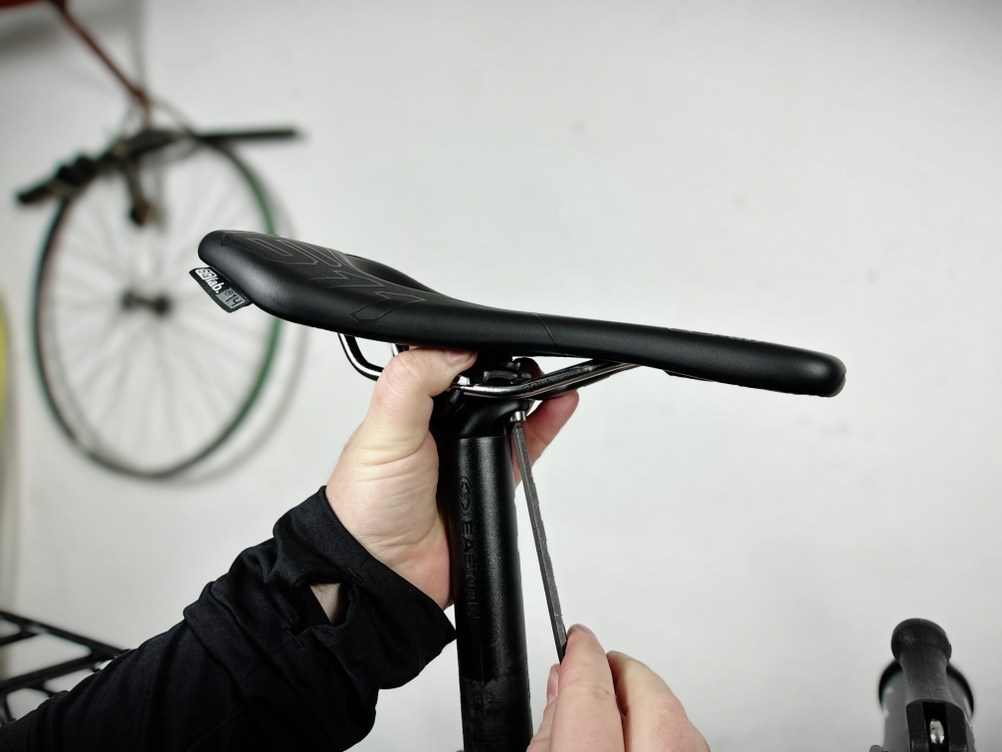 Der montierte SQlab 611 Ergowave CrMo ist in der Seitenansicht zu sehen. Eine Hand greift zur Befestigung unter dem Sattel.