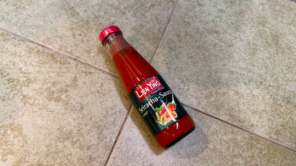 Auf einem Fließenboden liegt eine Sriracha-Sauce leicht schräg.