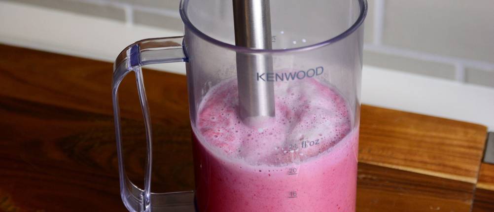 Stabmixer püriert einen rosa Smoothie in einem Messbecher.
