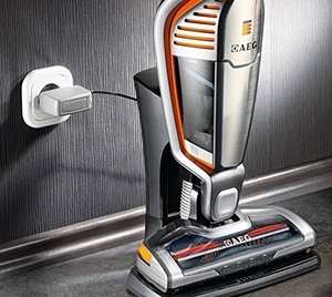 Der AEG-ECO-Li-35-Ergorapido-AG35POWER befindet sich in seiner Ladestation, die vor einer Wand mit einer Steckdose steht.