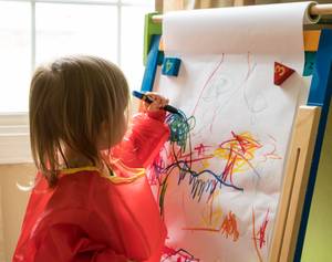 Staffelei-Kinder-Test: Kleines Kind malt mit Stift auf Papierrolle der Staffelei.