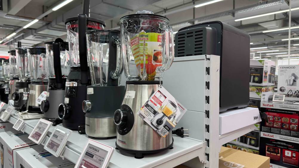 Ein getesteter Standmixer 1.000 Watt von schräg seitlich auf eine Verkaufsregal neben anderen Geräten.