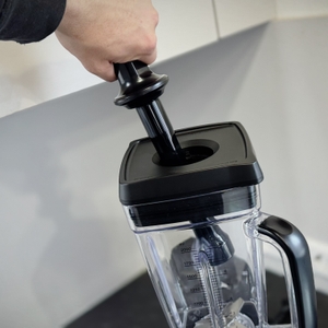 Eine Person führt den Stopfer in die Öffnung des getesteten Standmixers von Bosch ein.