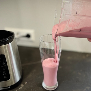 Eine Person schenkt aus dem getesteten Standmixer einen Milchshake in ein Glas.