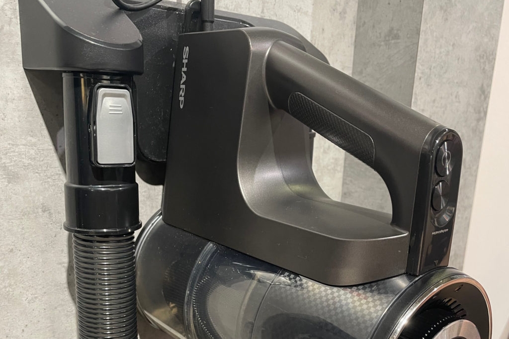 Der getestete Standstaubsauger lehnt an der Wand. Zu sehen ist der Griff und die Bedienelemente.