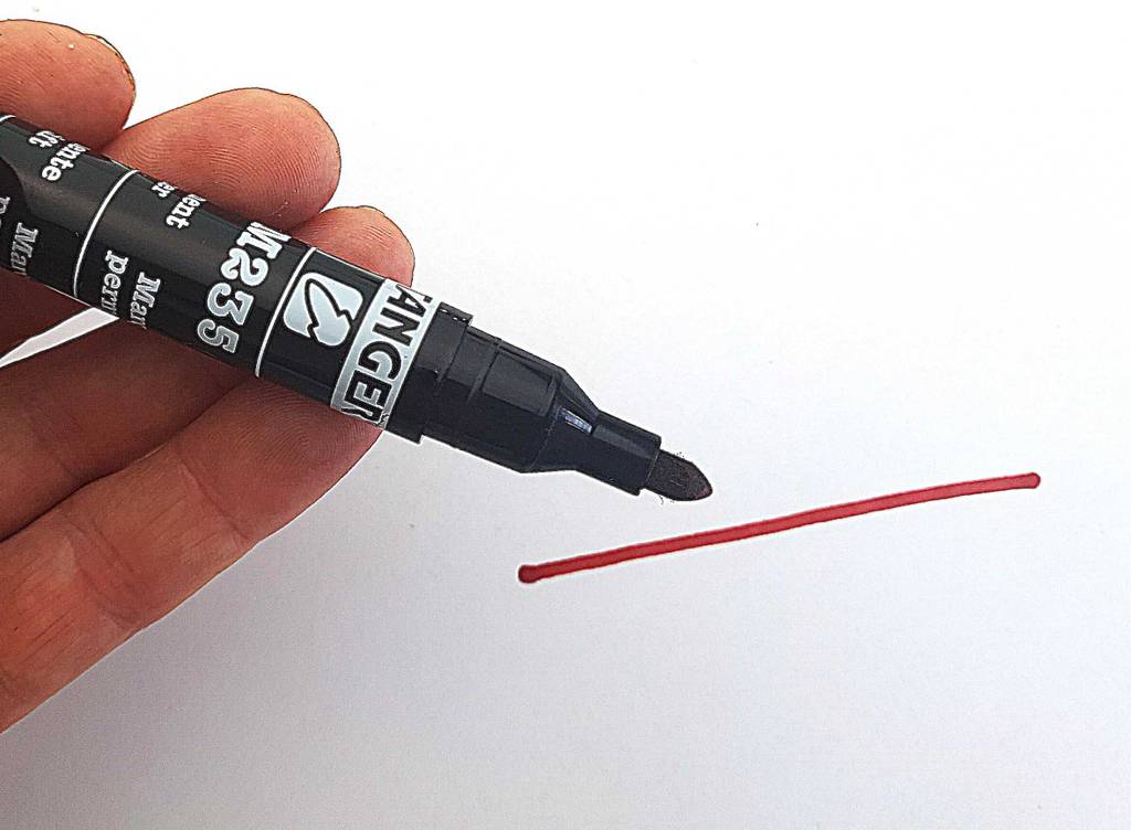 Über einem roten Strich auf weißer Oberfläche hält eine Hand den Alkoholmarker im Test