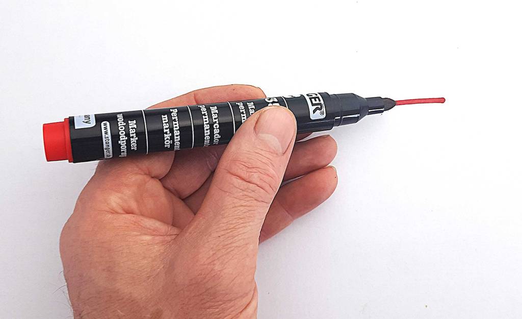 Alkoholmarker im Test: Eine Hand hält einen schwarzen Stift, mit dem ein roter Strich auf einer weißen Oberfläche gezogen wurde.