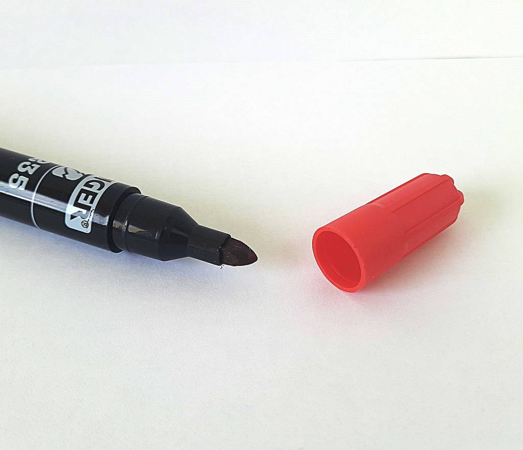 Der auf einer weißen Oberfläche liegende, getestete Alkoholmarker ist ein schwarzer Stift mit daneben liegender roter Verschlusskappe.