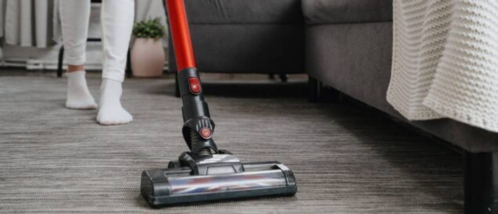 Vor einem Sofa wird mit einem elektrischen Standstaubsauger gereinigt